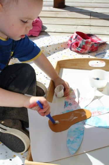 toddler gluing paper feathers on footprint turkey