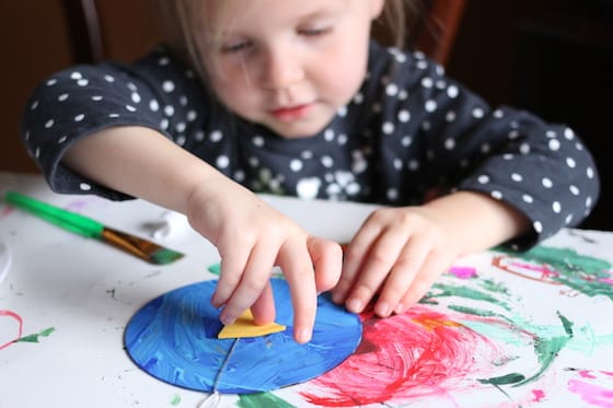 child gluing beak on a blue jay made from a cd