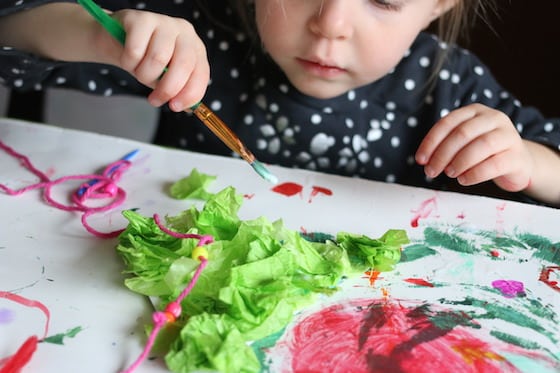 child gluing tissue paper to cardboard christmas tree