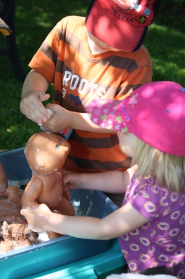 child squirting soap on doll for doll bath