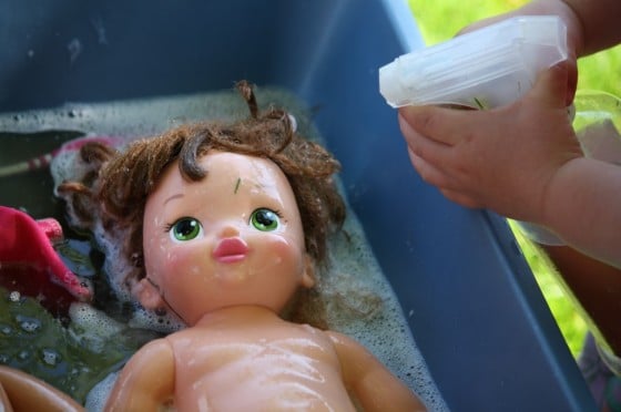 preschooler squirting doll with water from pump bottle