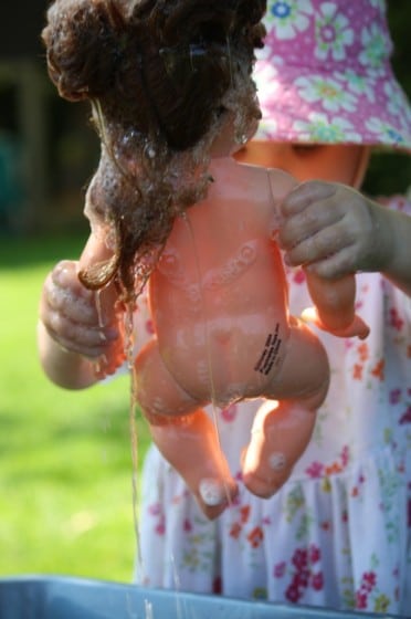 toddler holding doll over basin of water