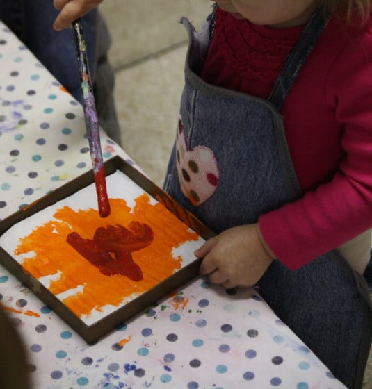 toddler painting orange and red in lid of box