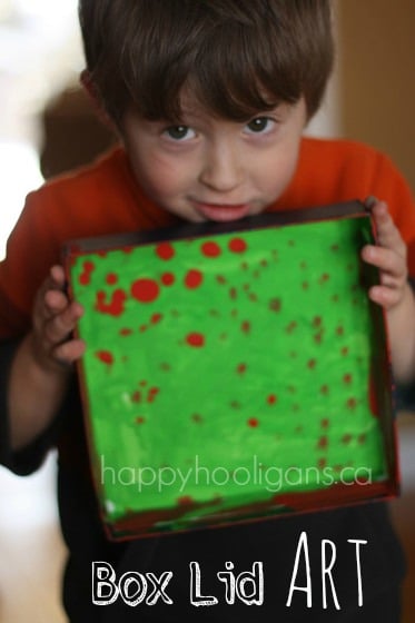 Preschooler holding green and red art painted in box lid