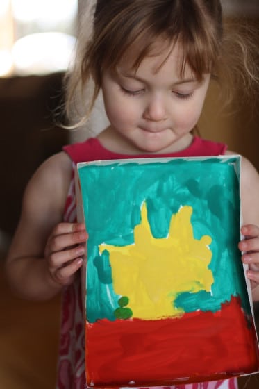 preschooler holding painting of yellow sun in box lid