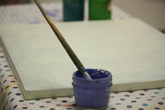 blue paint and paintbrush in front of primed canvas