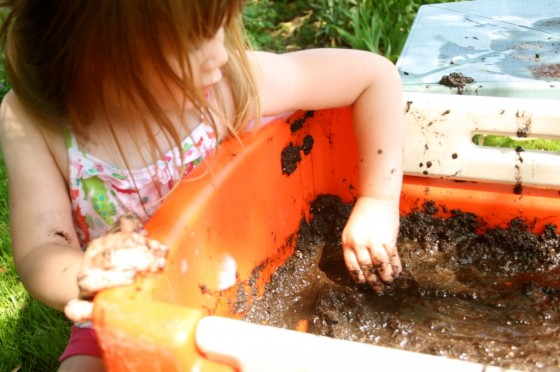 preschooler driving toy car in wagon filled with mud