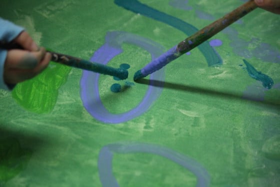 toddlers painting blue circles on green canvas