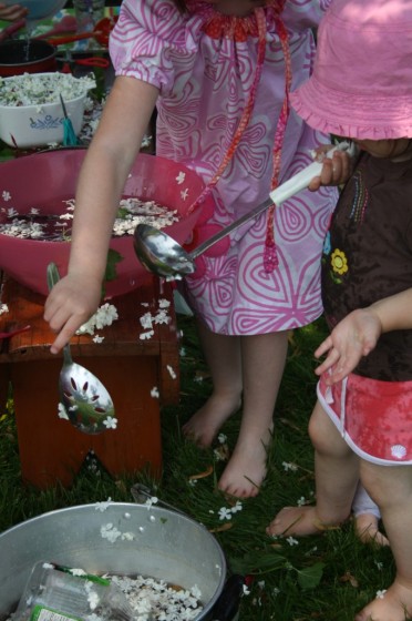 toddler holding ladle over bowl of flowers in water