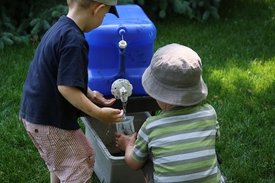 preschoolers filling measuring cup from blue camping jug in backyard