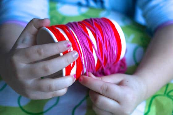 Child wrapping red and pink yarn around a cup