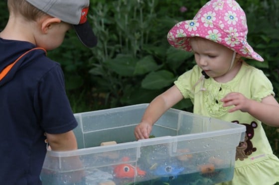 baby and toddler paying with bin filled with water and ocean toys