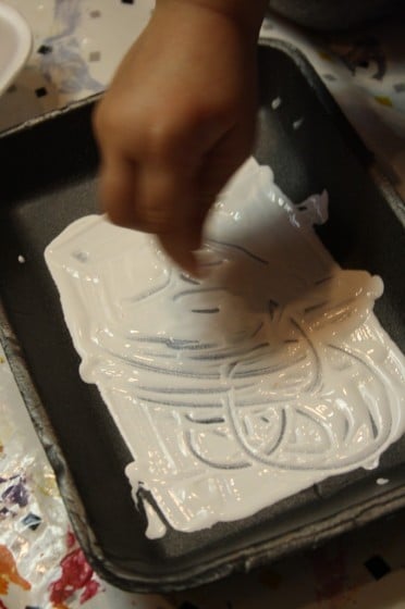 preschooler writing in white paint with a q-tip