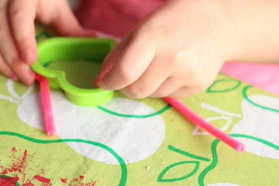 child wrapping pipe cleaner around heart shaped cookie cutter