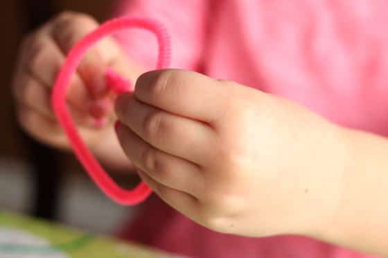 child forming pipe cleaner heart