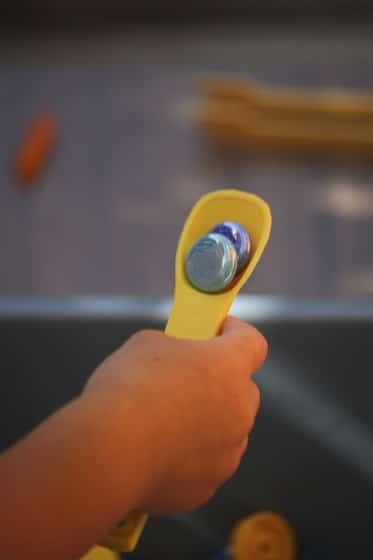 child transferring 2 glass bead on a small spoon