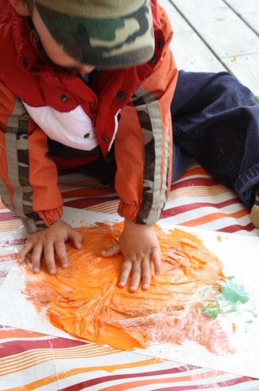 toddler smoosh painting a pumpkin with plastic wrap