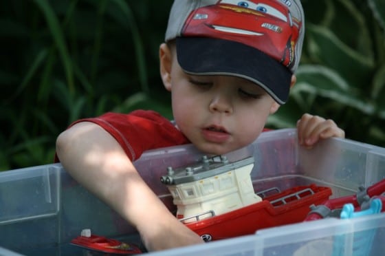 toddler boy playing with boats in bin of water