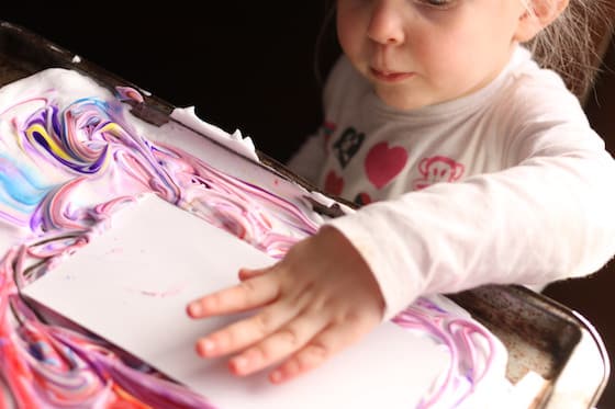 Child pressing paper into shaving cream and food colouring