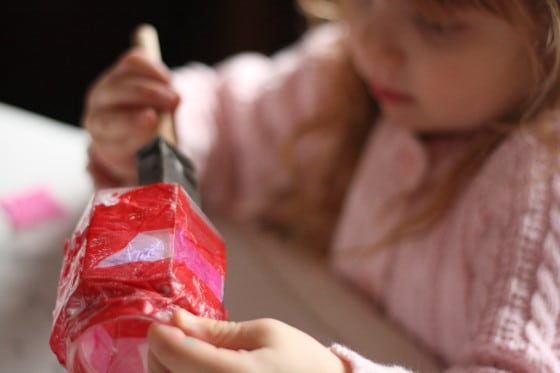 preschooler brushing glue over tissue paper on jar