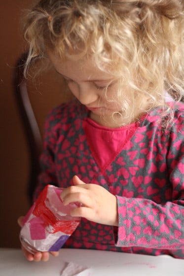 sticking red, pink and purple sucres of tissue paper to jar