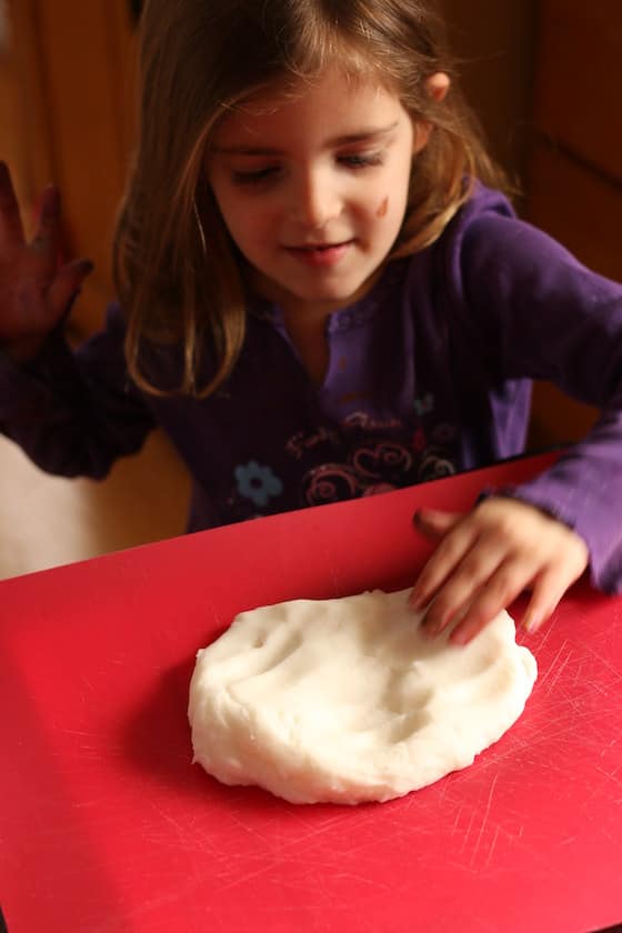 child kneading white clay dough on red cutting mat