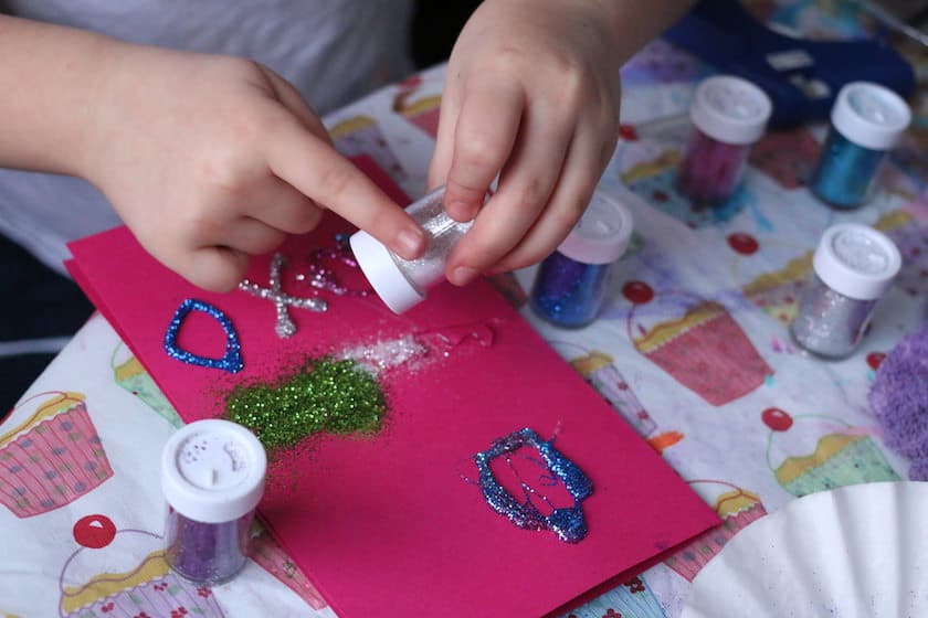 Child shaking glitter into hot glue