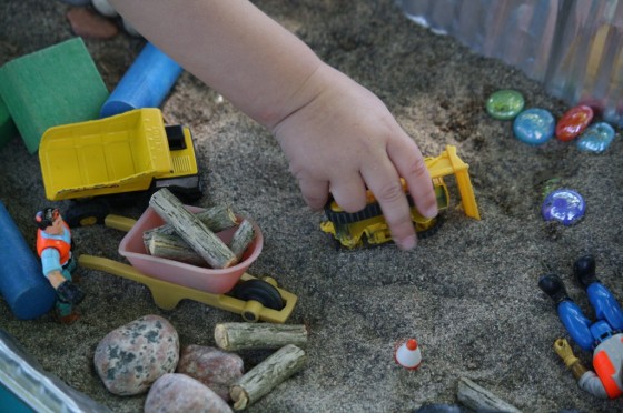 child pushing bulldozer in sand 