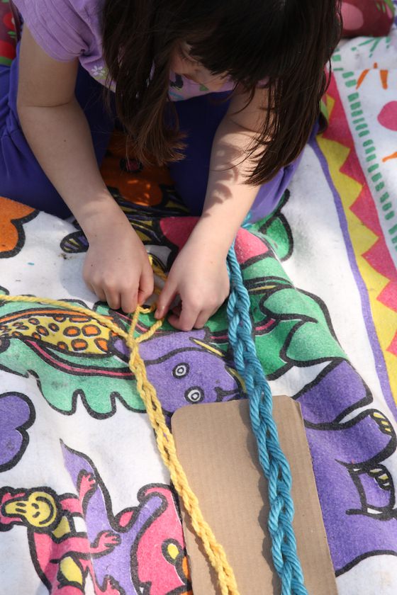 7 year old braiding yarn on a blanket in the backyard