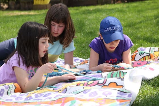 Kids lying on blanket in the grass, learning to braid