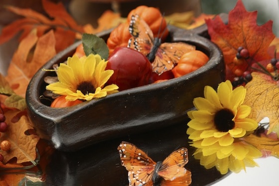 Wooden bowl filled with artificial sunflowers, pumpkins and apples on a mirrored fall sensory table