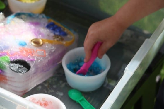 preschooler scooping blue salt on ice block with toys frozen inside