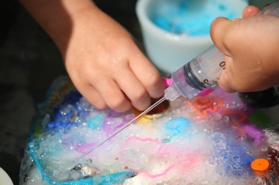 child spraying water on block of ice to get to toys inside 