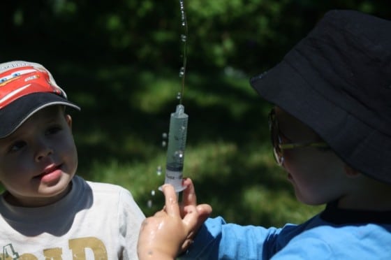 toddler watching preschooler squirt water with syringe