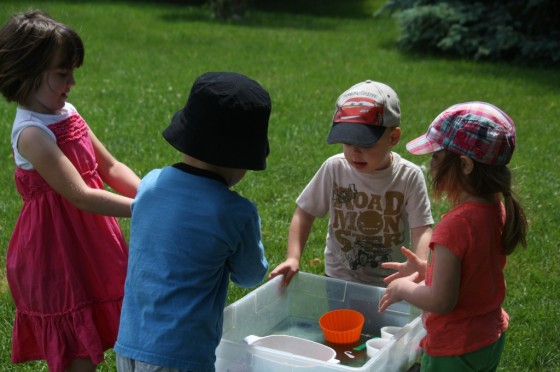 4 preschoolers gathered around ice age sensory bin in backyard