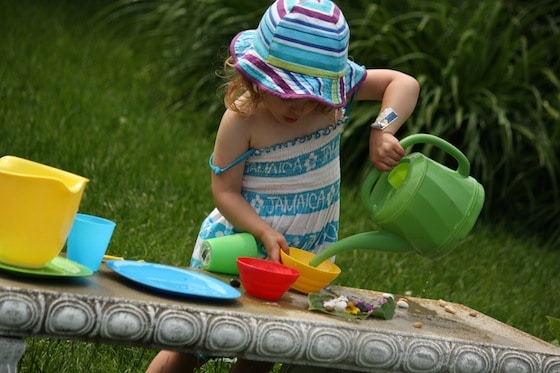 Toddler Pouring water out of green watering can, dishes for tea party