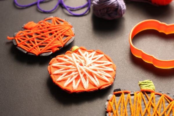 3 cardboard pumpkins wrapped in yarn displayed horizontally on black backdrop
