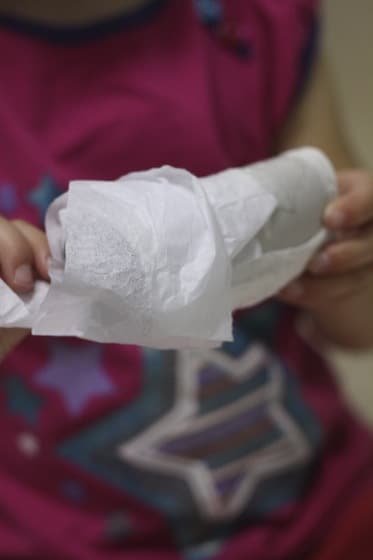 toddler wrapping tissue paper around toilet roll