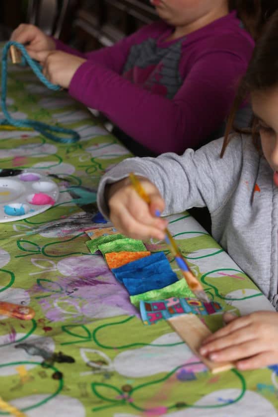 preschooler gluing fabric scraps to a paint stick