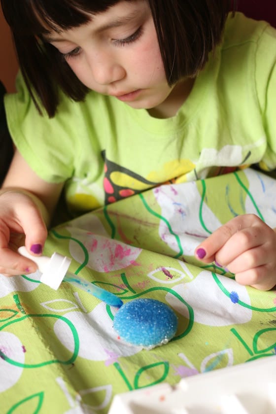 Child dripping blue watercolours on a rock covered in borax crystals