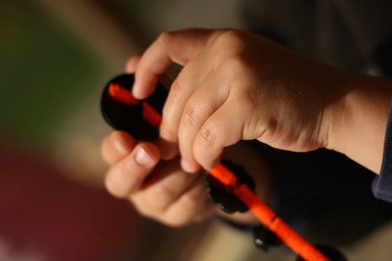 Child threading black buttons onto orange pipe cleaner