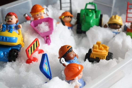 Little People and construction vehicles in a snow sensory bin