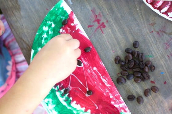 Preschooler gluing coffee beans on a paper plate watermelon