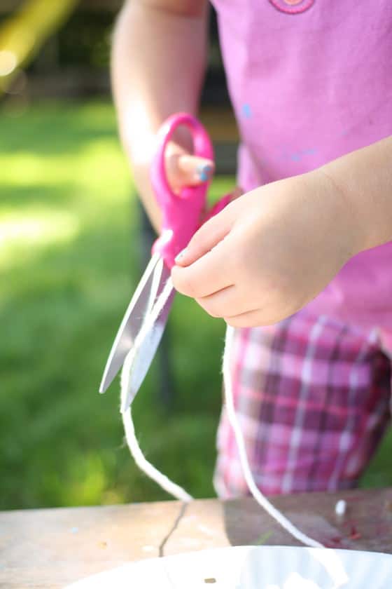 child cutting yarn with scissors for paper plate kite