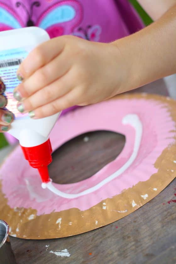 child squeezing glue onto paper plate