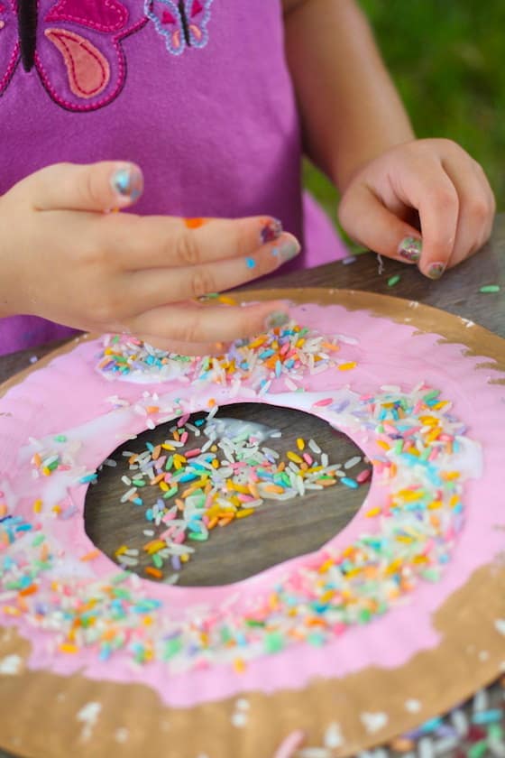 child sprinkling coloured rice onto a paper plate donut craft