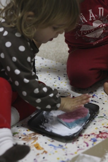 toddler and preschooler dipping sponge in white paint