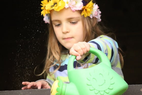 child watering flowers wearing hand made flowered tiara