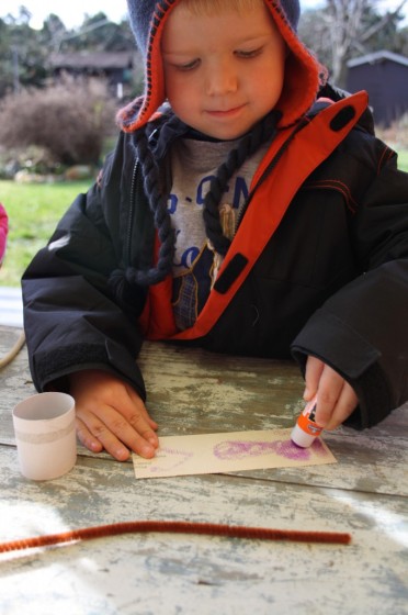 preschooler gluing paper around cardboard roll