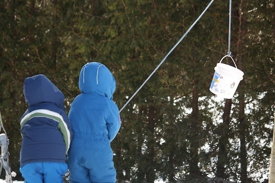 preschoolers in snow suits playing with bucket and rope contraption